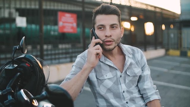 Young man motorcyclist talking on the phone while sitting on custom motorcycle
