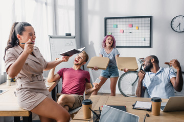 Selective focus of businesswoman holding pizza boxes near coworkers working in office