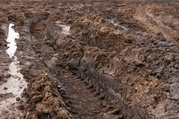 Texture of a dirty bad dirt road dirt road with puddles and clay drying mud with cracks and ruts. Off-road. The background.