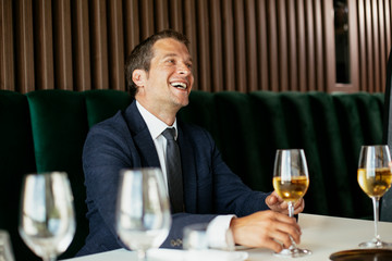 Handsome businessman dressed in the suit drinking wine. Businessman and businesswoman enjoying in the restaurant.