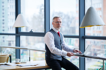 Adult male businessman, teacher, mentor working on a new project. Sits by a large window on the...