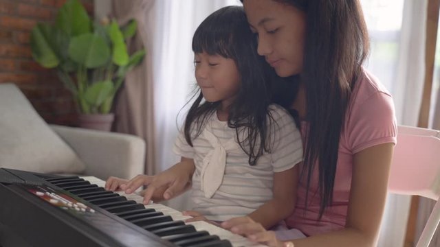 A child learn to play a musical instrument keyboard accompanied by her sister when sitting in a room at home
