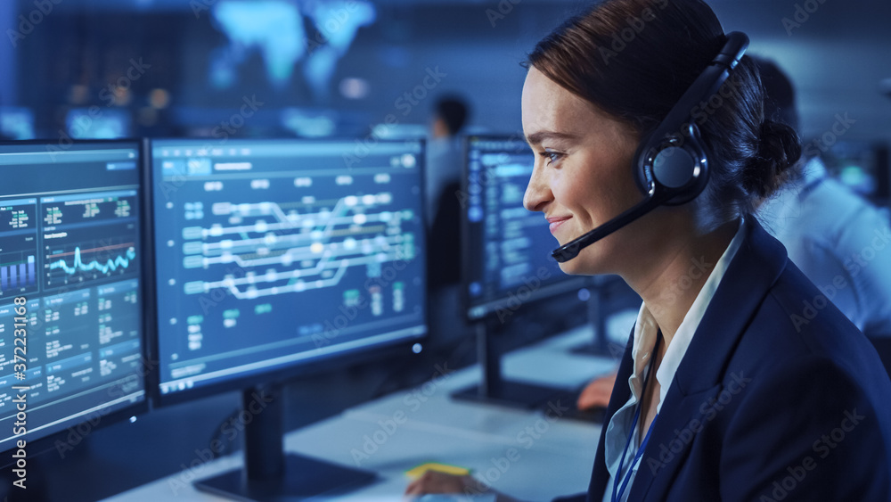Poster Beautiful Female Data Scientist Works on Personal Computer Wearing a Headset in Big Infrastructure Control and Monitoring Room. Woman Engineer in a Call Center Office Room with Colleagues.