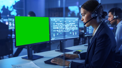 Confident Female Data Scientist Works on Personal Computer with Green Screen Mock Up in Big Infrastructure Control and Monitoring Room. Woman Engineer in Headset in Call Center Office with Colleagues.