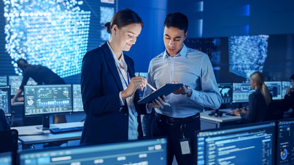 Project Manager and Computer Science Engineer Talking while Using A Digital Tablet Computer. Telecommunications Company System Control and Monitoring Office Room with Working Specialists.