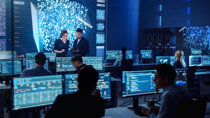 Project Manager and Computer Science Engineer Talking while Using A Digital Tablet Computer. Telecommunications System Control Monitoring Room with Neural Network on Big Screen.