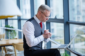 Adult male businessman, teacher, mentor working on a new project. Sits by a large window on the...