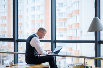 Adult male businessman, teacher, mentor working on a new project. Sits by a large window on the...