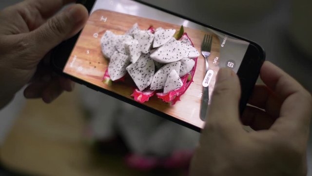 Woman's hands taking picture of prepared dragon fruit on wooden cutting board by using mobile phone. Food photography. Healthy eating. Camera app with thai language.