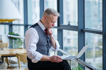 Adult male businessman, teacher, mentor working on a new project. Sits by a large window on the...