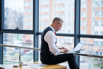Adult male businessman, teacher, mentor working on a new project. Sits by a large window on the...