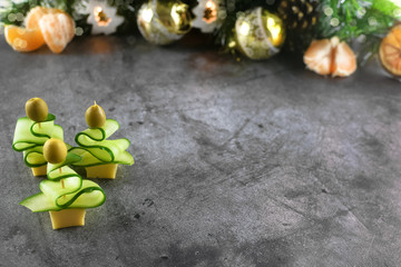 Christmas tree canape with a slice of cucumber, a slice of cheese and an olive for a festive Christmas snack. On a dark table against a background of festive decorations. Copy space. Mock up
