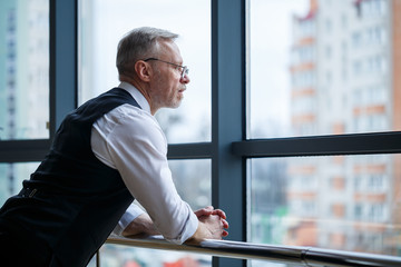 Smiling happy managing director thinks about his successful career development while stands in his...