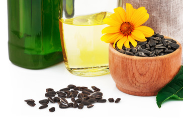 Sunflower oil in glass bottles, sunflower seeds in sack and rustic wooden bowl with flower and leaves on white background - 372236779