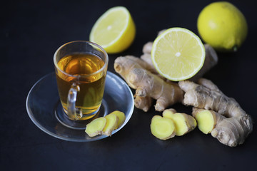 Ginger root whole and sliced. Ginger tea with lemon on the dark background. Fresh ginger root on stone background. Vitamins. Free space for your text.