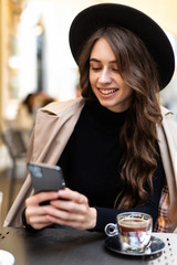 Portrait of beautiful girl wear in hat using her mobile phone in outdoors cafe.