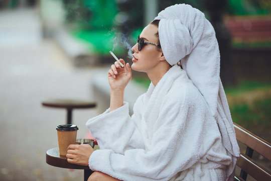 A girl in a robe drinks coffee and smokes a cigarette