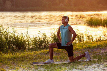 Sit up. A young athletic man working out, training listening to music at riverside outdoors. Concept of healthy lifestyle, wellness, sport, activity, weight loss. Inspired of nature, summertime.