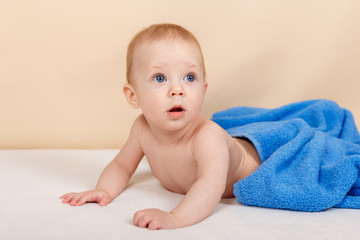 Adorable baby boy lying under the towel and having fun after bath