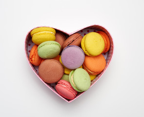 round baked multicolored macarons lie in a red cardboard box in the shape of a heart