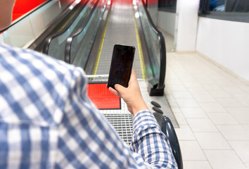 Hand holding mobile phone on escalator background. Concept of online ordering of goods with delivery via applications for mobile phone