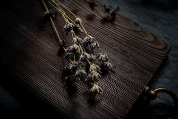 Dry lavender flowers on the old chopping board. Dark background for a culinary theme design.