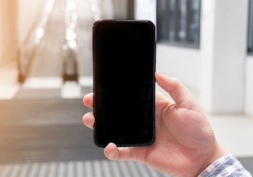 Hand holding mobile phone on escalator background. Concept of online ordering of goods with delivery via applications for mobile phone