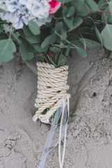 Beautiful close-up of maritime bride bouqet with sailor rope on sand background, northsea wedding decoration concept for beach ceremony.