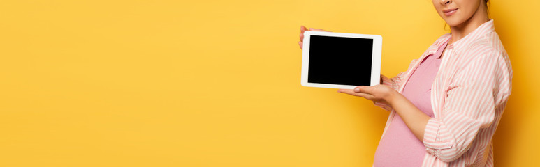 cropped view of young pregnant woman holding digital tablet with blank screen on yellow, horizontal image