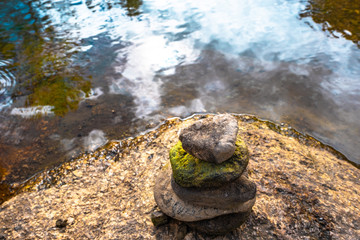 Fototapeta na wymiar zen stone, pyrimid stone on a rock near by river, green and peaceful nature background copy space.