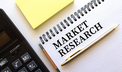 Notepad with text MARKET RESEARCH, next to it lies a calculator and yellow note papers. Business concept.
