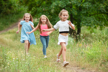 Obraz premium Memories. Kids, children running on green forest. Cheerful and happy boys and girs playing, laughting, running through green blooming meadow. Childhood and summertime, sincere emotions concept.