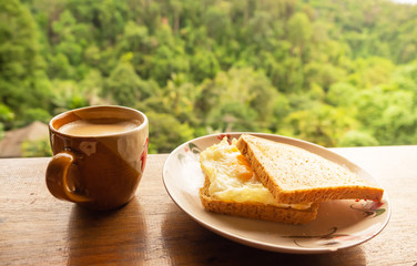 breakfast set on wooden table with lush forest background. coffee and bread eggs sanwish. copy-space