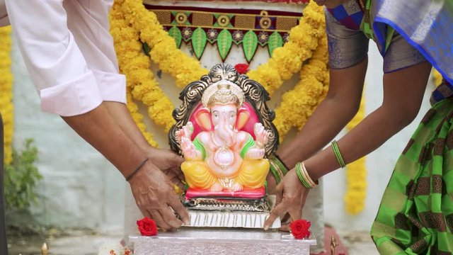 Senior Couples brought God ganesha idol and placing on decorated stage at home during vinayaka chaturthi festival - concept of Indian religious festival celebrations at home.