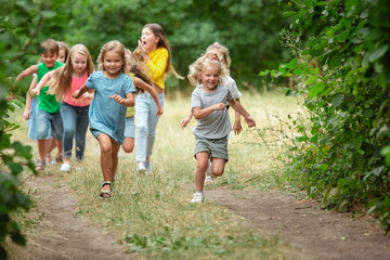 Obraz premium Happiness. Kids, children running on green forest. Cheerful and happy boys and girs playing, laughting, running through green blooming meadow. Childhood and summertime, sincere emotions concept.