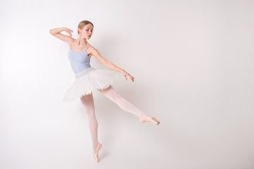 Young beautiful ballerina dances in big studio isolated on white background