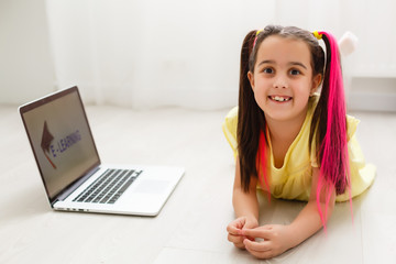 Cool online school. Kid studying online at home using a laptop. Cheerful young little girl using...