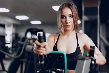 Fototapeta na wymiar Young beautiful woman training her arms in a gym apparatus