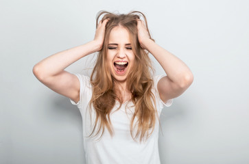 Fototapeta premium Angry young blong woman strong screaming with wide open mouth on light blue background. Closeup portrait