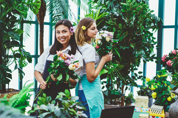 Portrait of funny female florist enjoying occupation in retail shop composing bouquets in friendly atmosphere,young multiracial employees of orangery enjoying creating floral composition together.