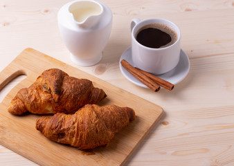 a white ceramic cup of black roasted coffee espresso and a french croissant on the wooden surface