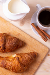 a white ceramic cup of black roasted coffee espresso and a french croissant on the wooden surface