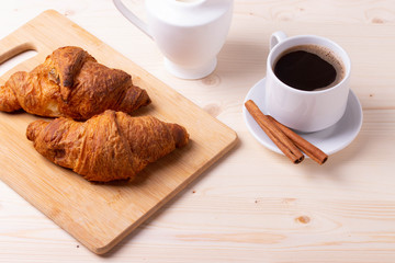 a white ceramic cup of black roasted coffee espresso and a french croissant on the wooden surface