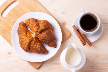 a white ceramic cup of black roasted coffee espresso and a french croissant on the wooden surface