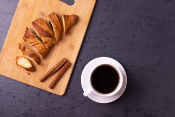 a white ceramic cup of black roasted coffee espresso and a french croissant on the wooden surface
