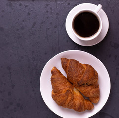 a white ceramic cup of black roasted coffee espresso and a french croissant on the wooden surface