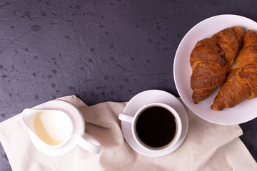 a white ceramic cup of black roasted coffee espresso and a french croissant on the wooden surface