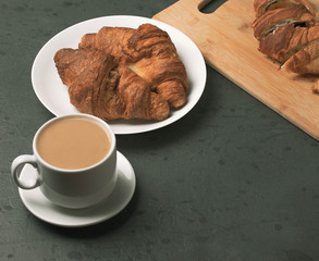 a white ceramic cup of black roasted coffee espresso and a french croissant on the wooden surface