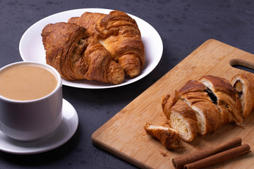 a white ceramic cup of black roasted coffee espresso and a french croissant on the wooden surface