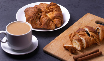 a white ceramic cup of black roasted coffee espresso and a french croissant on the wooden surface